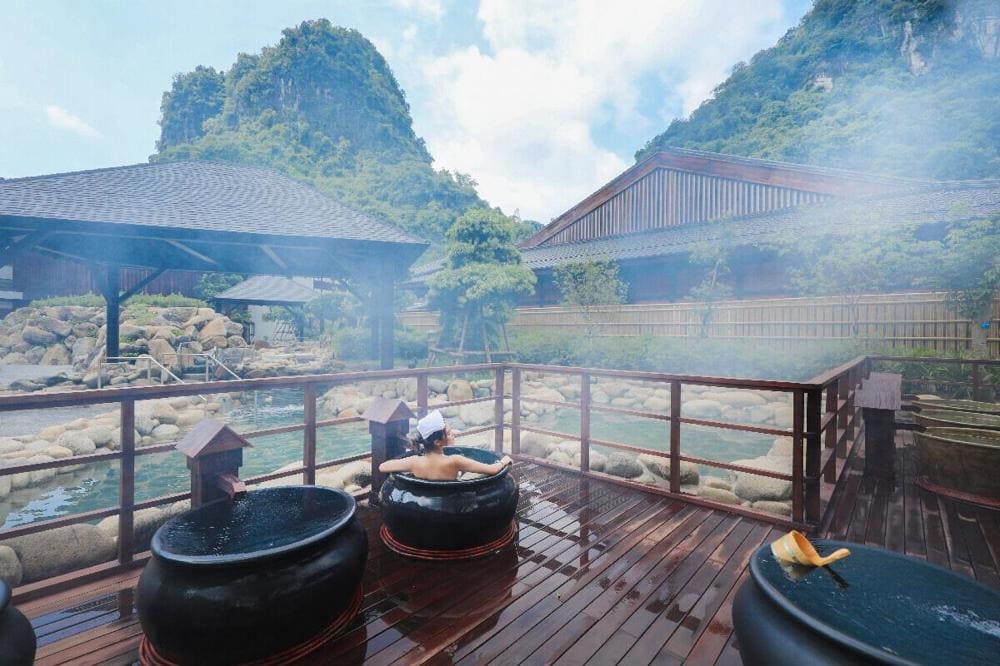Steam rises from a mineral hot spring nestled in a rainy mountain landscape